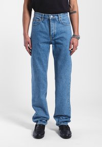 Světle modré denimové džíny s rovnými nohavicemi, vysokým pasem a jemným vyblednutím. Obsahují klasický pětibodový styl a kovové detaily.