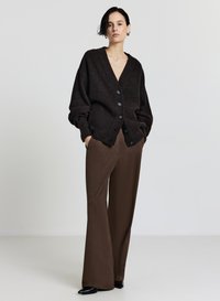 Brauner Strickcardigan mit tiefem V-Ausschnitt, oversized Passform, sechs dunklen Knöpfen und gerippten Ärmeln, kombiniert mit braunen, hochtaillierten Schlaghosen.