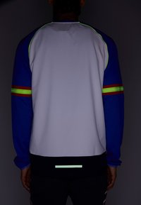 Kolorowa sportowa bluza z niebieskimi rękawami, szarym korpusem, odblaskowymi akcentami oraz minimalistycznym wzorem pasków na dole.