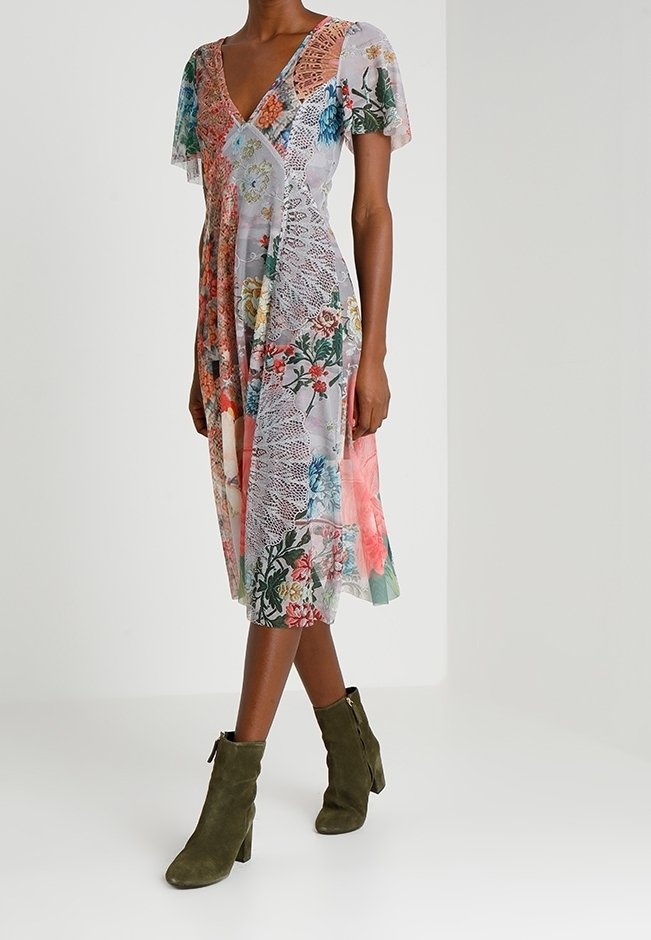 Femme portant une robe patchwork florale courte aux genoux, à manches courtes, associée à des bottines en daim vert olive.
