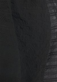 Czarna tkanina z teksturowanymi wzorami, z mieszanką gładkich i pogniecionych sekcji, tworząca warstwowy wygląd. Widoczne cienkie, przezroczyste akcenty.