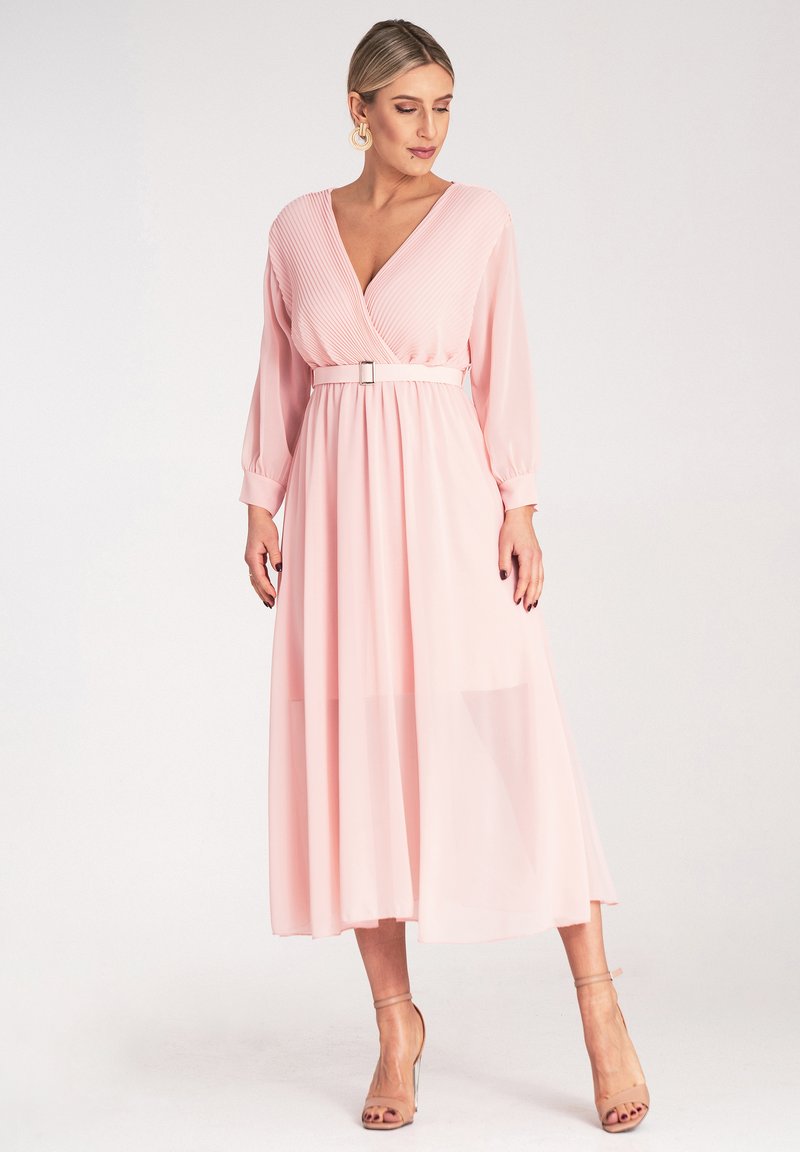 Maxi sukienka w delikatnym różu, z plisowanym dekoltem w kształcie litery V, długimi rękawami, przewężoną talią z metalowym paskiem oraz zwiewną, przezroczystą spódnicą.