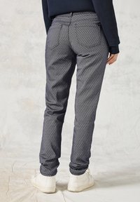 Strak passende marineblauwe broek met een ruitpatroon, voorzien van achterzakken. Gecombineerd met witte sneakers, getoond vanuit de achterkant.
