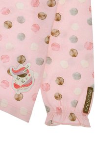 Helles rosa Gewebe mit verschieden großen Punkten in Pastellfarben. Mit einem Einhorn-Patch und gerafften Ärmelbündchen. Markenetikett sichtbar.