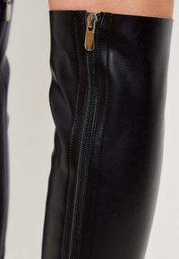 Black leather thigh-high boot with a smooth texture, featuring a side zipper and stitched seams for a fitted design.