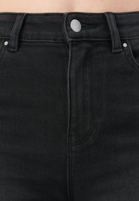 Jeans neri in denim a vita alta con un design a cinque tasche, chiusura con bottone in metallo e cuciture a contrasto lungo le cuciture e le tasche.