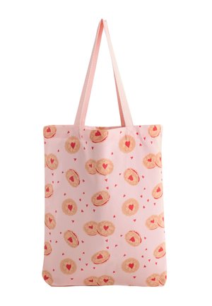 Vaaleanpunainen ostoskassi pitkillä kahvoilla, koristeltu pyöreiden pikkuleipien kuviolla, joissa on punaiset sydämet keskellä ja pieniä ripoteltuja sydämiä.