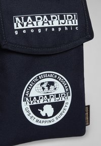 Primo piano di una borsa in tessuto nero con il logo geografico bianco Napapijri e l'emblema del programma di ricerca antartico, che presenta un globo e il contorno dei continenti.