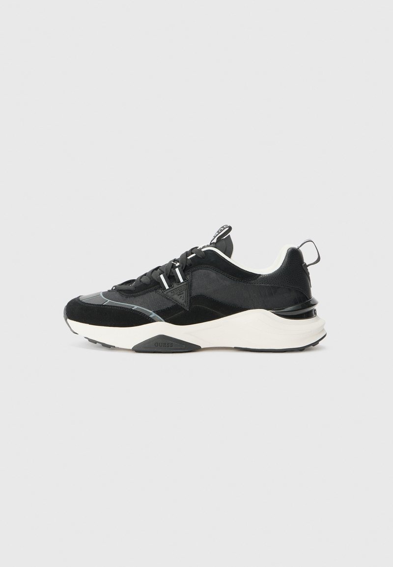 Black sneaker featuring a mix of suede and mesh materials, chunky white sole, and reflective accents. Lace-up design with a pull tab.