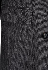 Vlněný kabát s houndstooth vzorem, který má černý knoflík, diagonální herringbone vzor v šedé a bílé barvě a design kapsy s klopou.