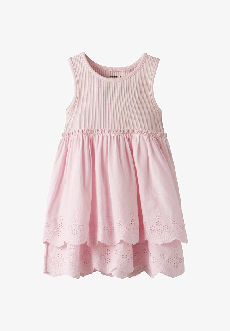 Robe sans manches rose avec un corsage côtelé et une jupe superposée ornée de motifs floraux découpés sur l'ourlet. Tissu doux avec un design fluide.