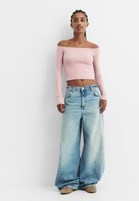 Svetloružový crop top s dlhými rukávmi a voľným strihom, ktorý sa nosí na ramene, skombinovaný s širokými svetlomodrými džínsami. Textúrovaná tkanina a voľný strih.