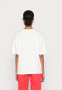 Camiseta blanca de algodón con mangas cortas y cuello redondo, combinada con pantalones rojos brillantes. Diseño minimalista, textura lisa.