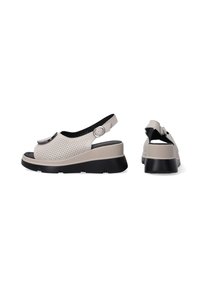 Beige perforerede sandaler med sort sål, slingback-rem og cirkulært hardware-detalje. Tekstureret mellemsål tilføjer højde.