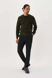 Green knit sweater, black trousers, and black loafers. Smooth texture, fitted design, and crew neckline. Simple and modern appearance.