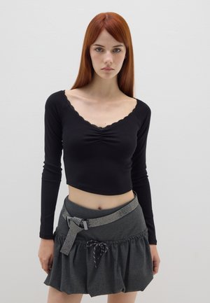Zwarte lange mouw cropped top met kantafwerking, gecombineerd met een donkergrijze rok met een gerimpelde zoom en een metallic riem met een gesp.