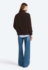 Brown ribbed-knit sweater with a high collar, paired with light blue wide-leg jeans. Visible texture and layering details. Loose fit.