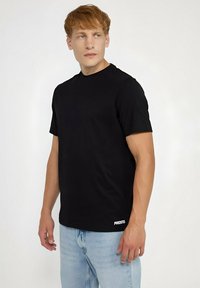 Czarny t-shirt z krótkim rękawem wykonany z gładkiego materiału, z okrągłym dekoltem i subtelnym logo na dolnym brzegu, w połączeniu z jasnoniebieskimi dżinsami.