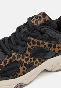 Baskets noires avec un mélange de mesh et d'accents en daim imprimé léopard. Lacets épais et semelle texturée avec une semelle intermédiaire beige contrastante.