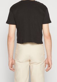 Sort cropped ribbet t-shirt med korte ærmer, rund halsudskæring og en tekstureret stof. Parret med beige bukser, vist bagfra.