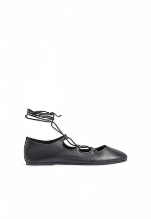 Ballerines en cuir noir avec un bout pointu, des sections découpées et de fines lacets enroulés autour de la cheville ; texture lisse.