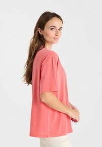 T-shirt en coton corail à manches courtes et coupe décontractée. Texture douce, col rond et coutures décoratives au niveau des coutures des épaules.