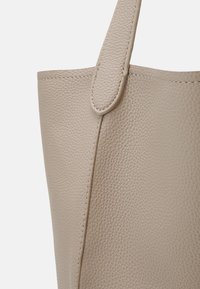 Béžová kožená taška přes rameno s texturovaným povrchem, vybavená jedním uchytem a viditelným prošíváním podél hran. Jednoduchý a funkční design.