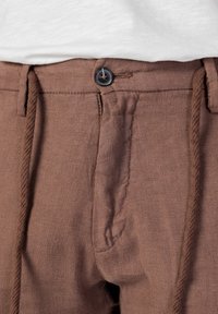 Hnědé lněné kalhoty s jemnou texturou, vybavené šňůrkou v pase, knoflíkovým zapínáním a předními kapsami. Ležérní a lehký design.