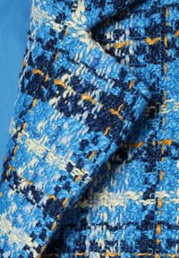 Tela texturizada en varios tonos de azul, con un patrón tejido que presenta acentos en amarillo y crema. Muestra un diseño rústico y táctil.