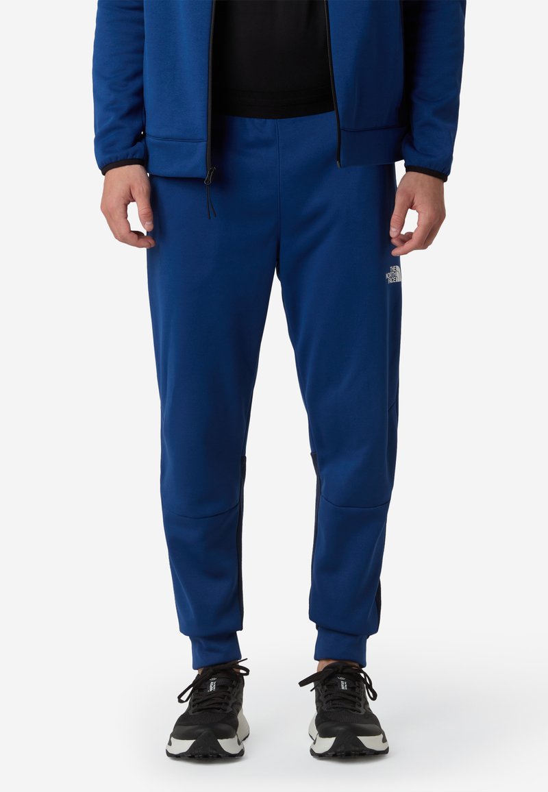 Niebieskie sportowe joggery wykonane z gładkiego materiału, z bocznymi kieszeniami na zamek, elastycznymi mankietami i detalem logo na udzie.