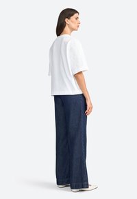 T-shirt blanc à manches courtes avec une coupe décontractée, associé à un jean évasé bleu foncé. Le jean présente une coupe droite et un ourlet propre.