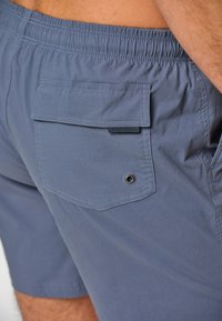 Shorts de bain bleus avec une taille élastique, une poche patch au dos et un œillet en métal. Tissu lisse et léger.