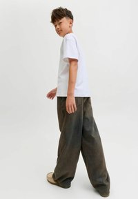 Bijela majica s kratkim rukavima u kombinaciji sa slobodnim, izblijedjelim maslinasto zelenim hlačama. Outfit se ističe opuštenim krojem i jednostavnim dizajnom.