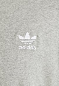 Pelēka kokvilnas T-kreklu ar baltu izšūtu "adidas" logotipu un trim lapu formas akcentiem. Mīksta tekstūra ar klasisku piegriezumu.