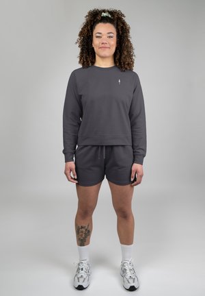 Gray sweatshirt with long sleeves, round neckline, and logo on chest; matching gray shorts; model wears white socks and silver sneakers.