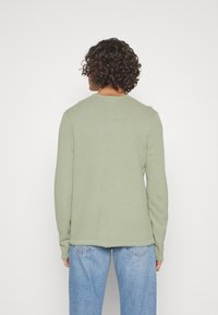 Un pull vert clair à manches longues en maille texturée, avec un col rond et une coupe décontractée, associé à un jean en denim clair.