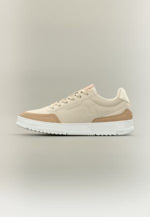 Baskets à tige synthétique beige avec des accents en daim, semelle blanche, languette de talon rose contrastante et détails texturés sur les côtés.