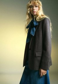 Brązowa marynarka w kratę o strukturalnym kroju, z denimsowym krawatem w kształcie kokardy. W połączeniu z niebieską spódnicą dżinsową, gładkie faktury przez całą stylizację.