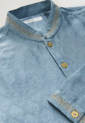 Chemise bleu clair avec un motif en relief, présentant une couture dorée décorative sur le col et des boutons avec une finition dorée.