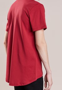 Camiseta corta de manga corta roja, hecha de algodón, con dobladillo redondeado y textura suave, con un corte relajado y detalles de costura mínimos.