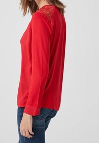 Rode top met lange mouwen en kantaccenten op de schouders, met een soepele textuur en een relaxte pasvorm, gecombineerd met blauwe denim jeans.