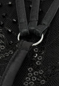 Zwarte mesh stof met een metalen ring, gekleurde details en banden. De textuur is ingewikkeld met kleine pailletten die in het materiaal zijn verwerkt.
