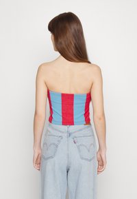 Top strapless listrado em vermelho e azul com um design justo, feito de um tecido leve; combinado com jeans de cintura alta em azul claro.