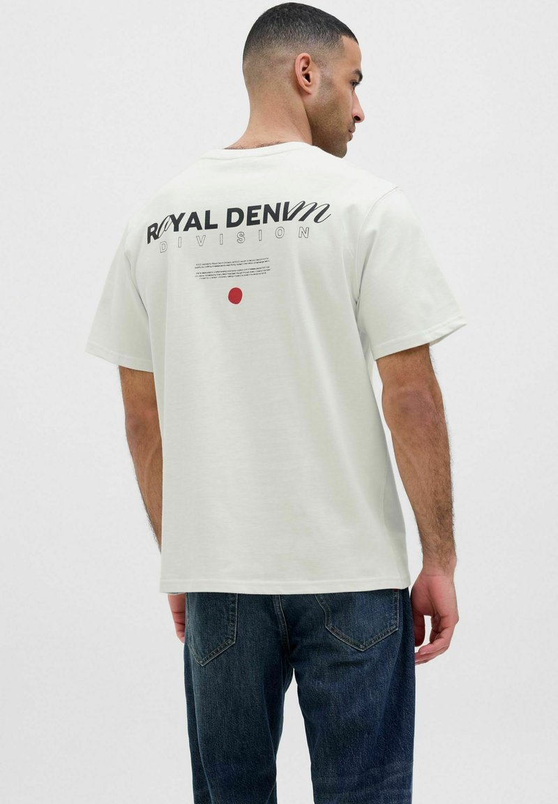 Korte mouwen beige t-shirt met zwarte en rode tekst op de achterkant, met een losse pasvorm en standaard ronde hals.