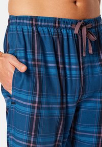 Szorty wypoczynkowe w kratę w kolorze niebieskim, z fioletowymi i czarnymi liniami. Elastyczny pas z troczkiem i boczne kieszenie. Miękka faktura tkaniny.