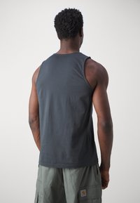 Mørk grå tank topp laget av bomull. Har en klassisk passform med rund hals og brede armhull, båret med lysegrønne cargo shorts.