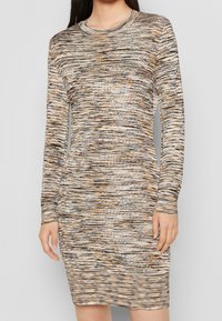 Stickad klänning med långa ärmar, med ett flerfärgat abstrakt mönster i beige, brunt och orange, med en figurnära silhuett och rundad halsringning.