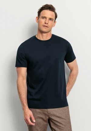 Marineblaues T-Shirt mit kurzen Ärmeln aus weicher Baumwolle. Es verfügt über einen runden Ausschnitt und eine glatte Textur und wird mit braunen, strukturierten Hosen kombiniert.