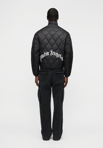 Μαύρο μπουφάν bomber με καπιτονέ, με ψηλό γιακά και το λογότυπο «Palm Angels» σε λευκό στην πλάτη. Φορεμένο με μαύρο παντελόνι cargo.
