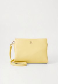Gul lædertaske med aftagelig rem, der har en glat tekstur og en metallisk logoaccent på fronten.